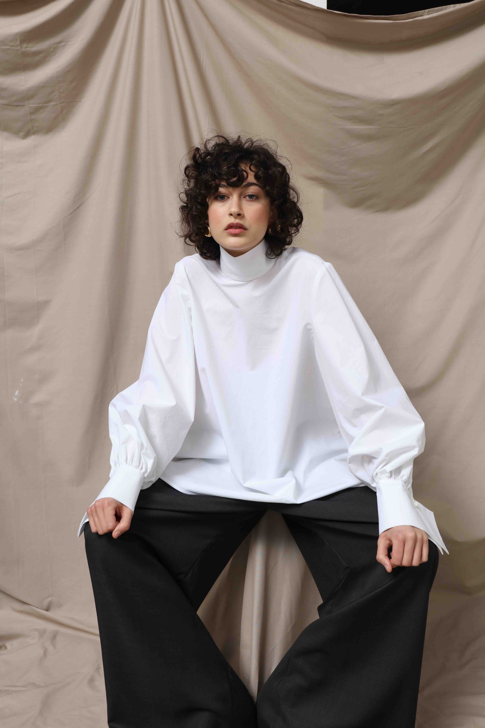 Regula Blouse by House of Woven Stories, handcrafted in Italy from 100% organic cotton poplin. Features adjustable long bow, minimalist tailoring, and sustainable design inspired by global craftsmanship.