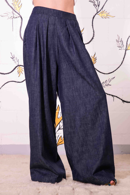 Model is wearing dark denim wide-leg trousers made from 100% Italian cotton, featuring a mid-rise elastic waistband, front pleats, and side pockets.