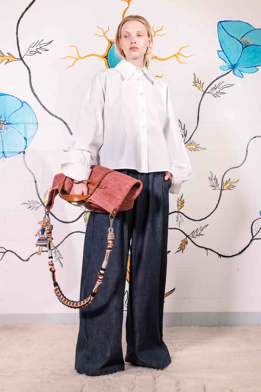 Model is wearing dark denim wide-leg trousers made from 100% Italian cotton, featuring a mid-rise elastic waistband, front pleats, and side pockets.