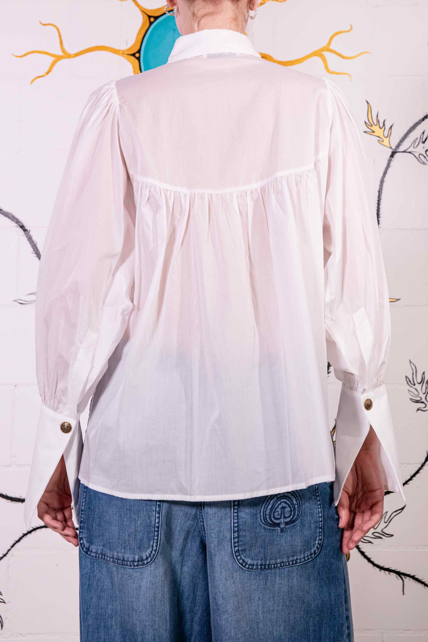 Model is wearing a white V-neck cotton blouse with relaxed fit, wide cuffs, and vintage button detail by House of Woven Stories.