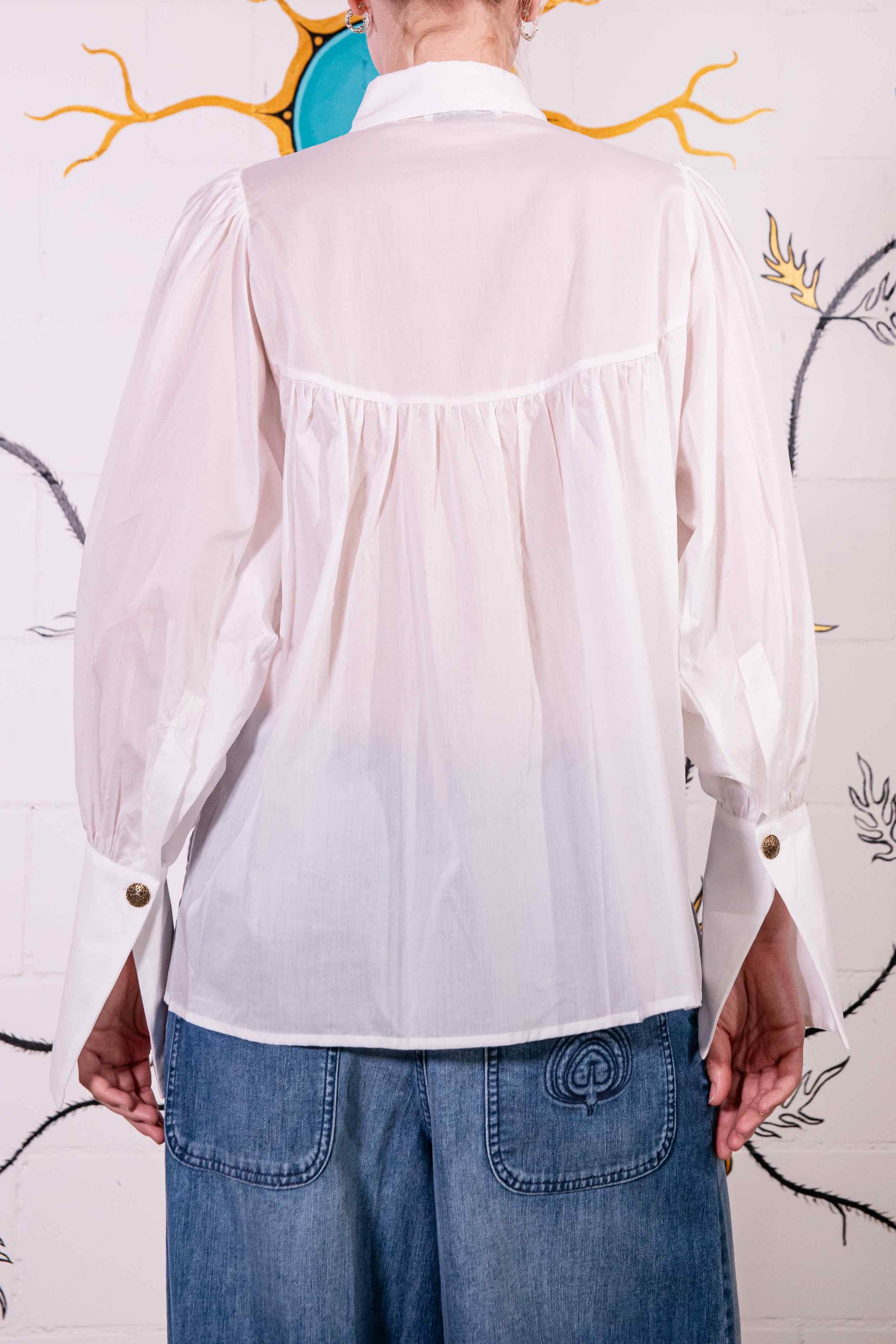Model is wearing a white V-neck cotton blouse with relaxed fit, wide cuffs, and vintage button detail by House of Woven Stories.