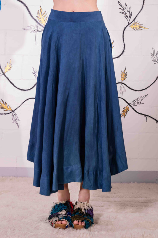 Model is wearing an indigo wrap skirt in naturally dyed silk by A Sacred Wrap, featuring a fluid bias cut, elasticated waistband, and side pockets. Part of House of Woven Stories selection.