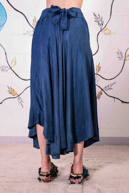 Model is wearing an indigo wrap skirt in naturally dyed silk by A Sacred Wrap, featuring a fluid bias cut, elasticated waistband, and side pockets. Part of House of Woven Stories selection.