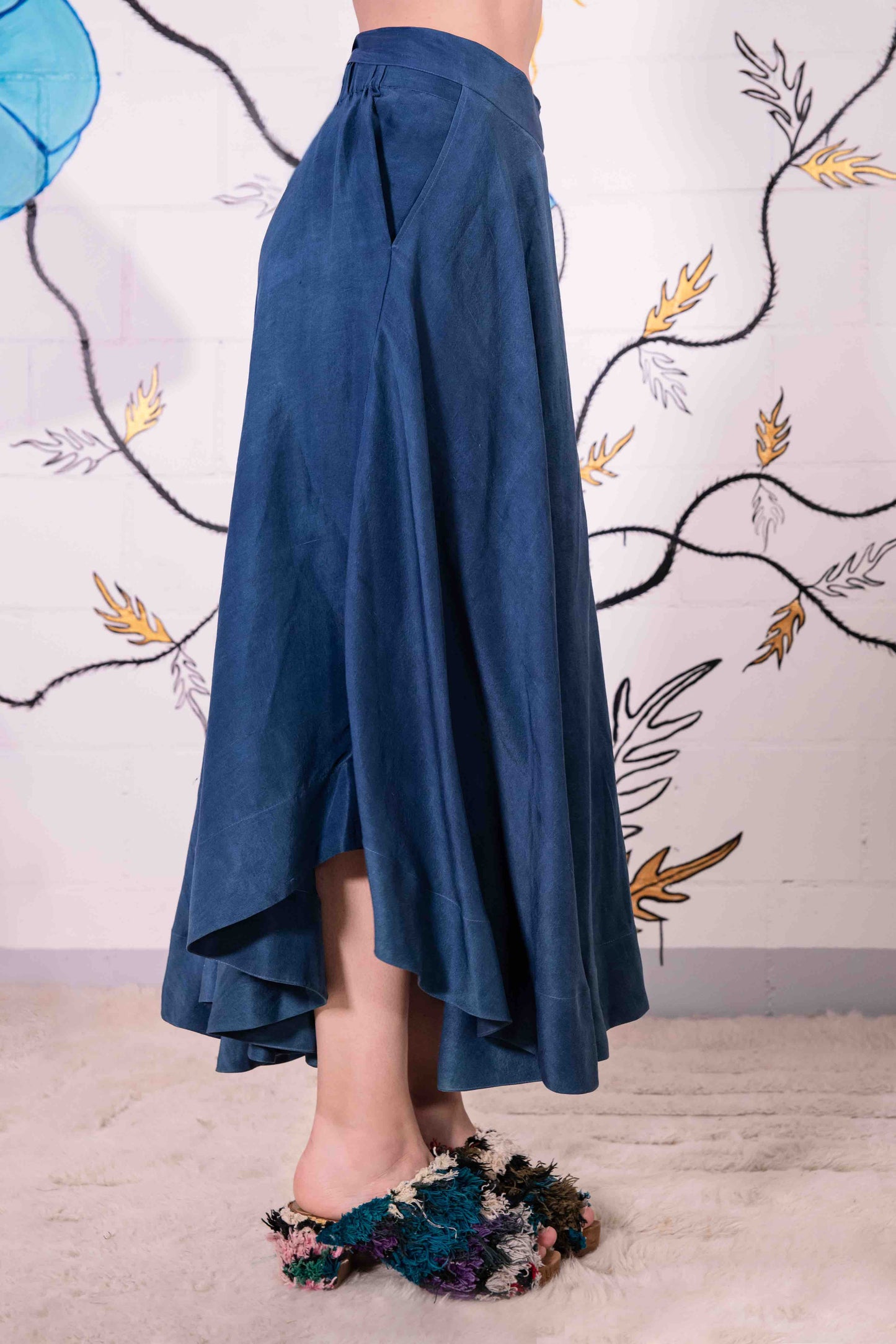 Model is wearing an indigo wrap skirt in naturally dyed silk by A Sacred Wrap, featuring a fluid bias cut, elasticated waistband, and side pockets. Part of House of Woven Stories selection.