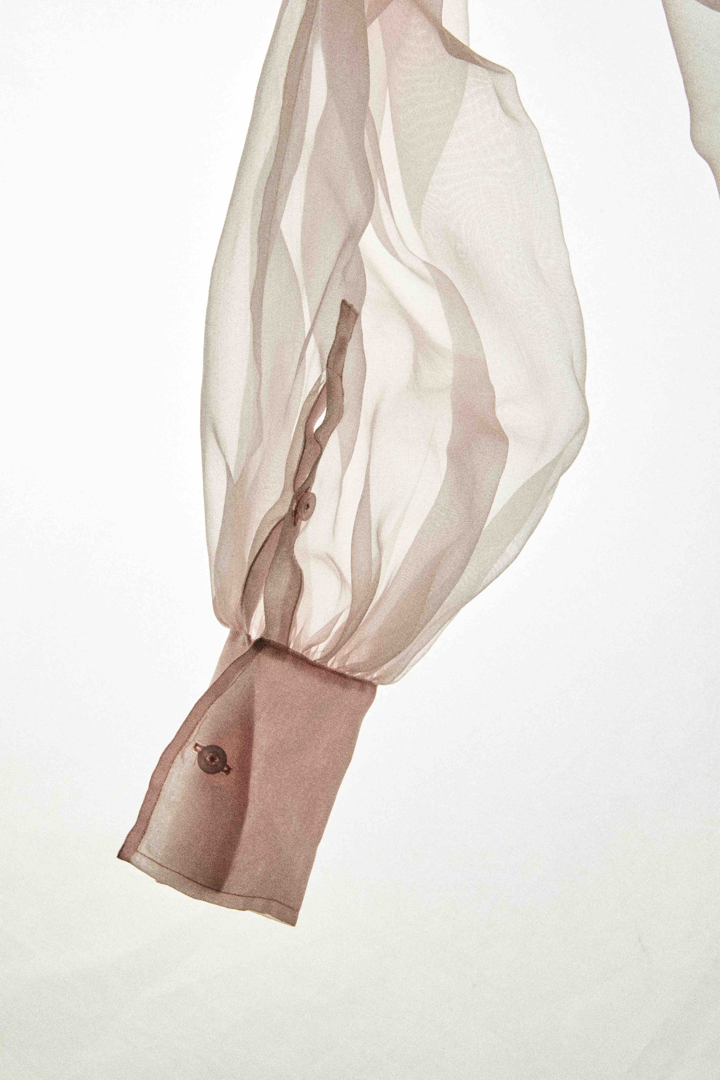 Model wearing a pink silk organza shirt by Abadia from the House of Nomad Stories collection, featuring sheer balloon sleeves and a lightweight structured silhouette in an elegant minimal setting.