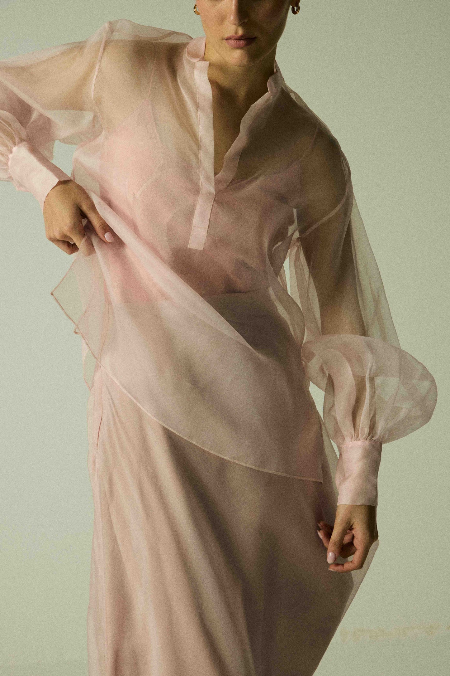 Model wearing a pink silk organza shirt by Abadia from the House of Nomad Stories collection, featuring sheer balloon sleeves and a lightweight structured silhouette in an elegant minimal setting.