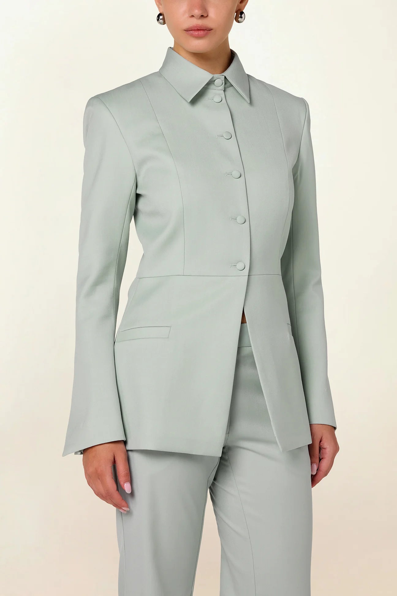 Model wearing a green tailored collared blazer by Abadia from the House of Nomad Stories collection, featuring a structured wool blend fabric, sharp collar, fitted silhouette, and clean minimal tailoring.