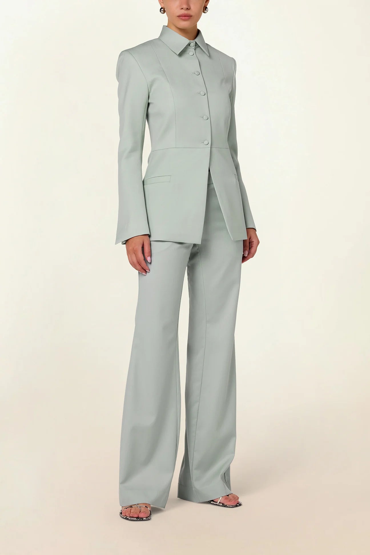 Model wearing a green tailored collared blazer by Abadia from the House of Nomad Stories collection, featuring a structured wool blend fabric, sharp collar, fitted silhouette, and clean minimal tailoring.
