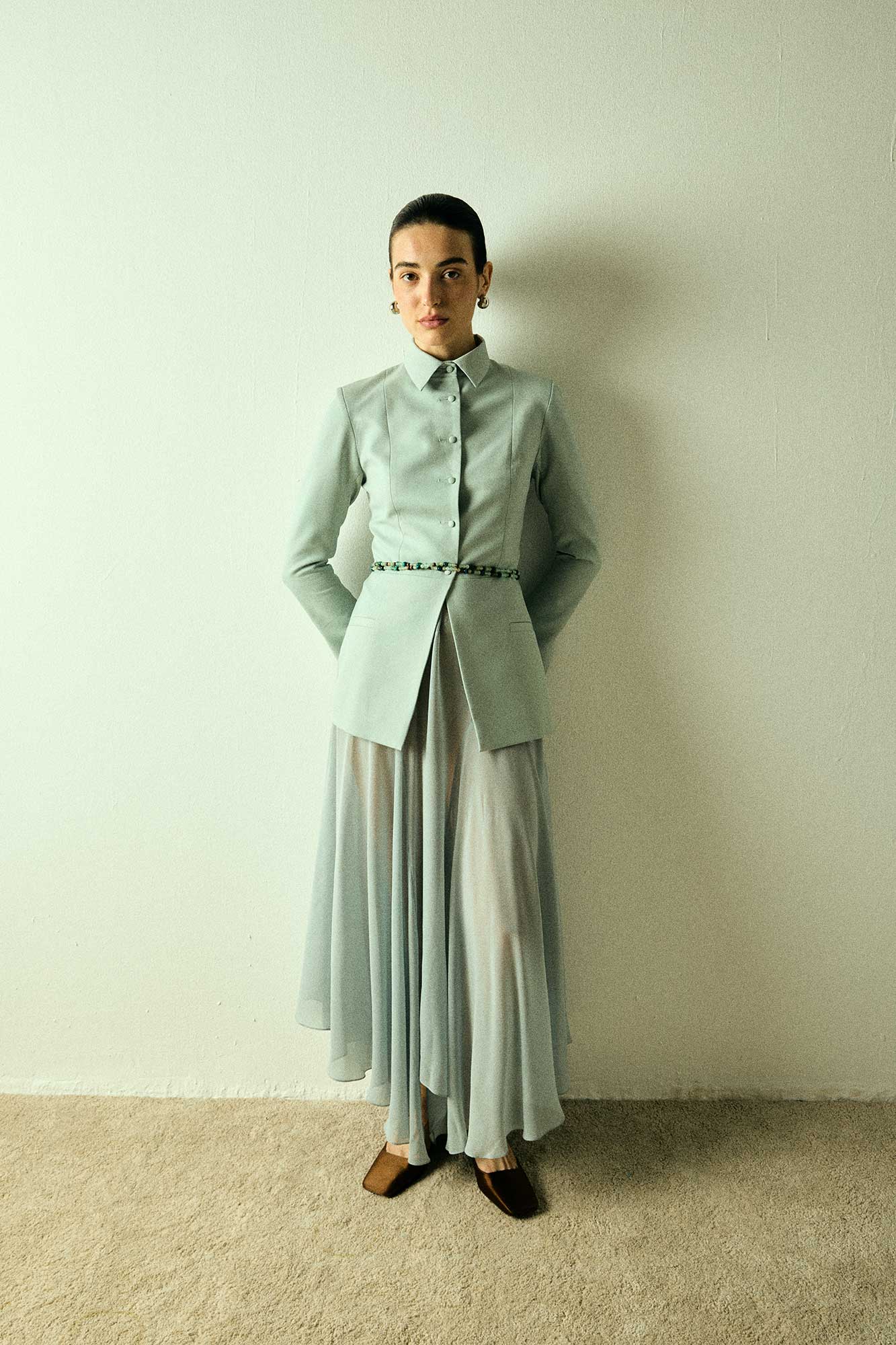 Model wearing a green tailored collared blazer by Abadia from the House of Nomad Stories collection, featuring a structured wool blend fabric, sharp collar, fitted silhouette, and clean minimal tailoring.