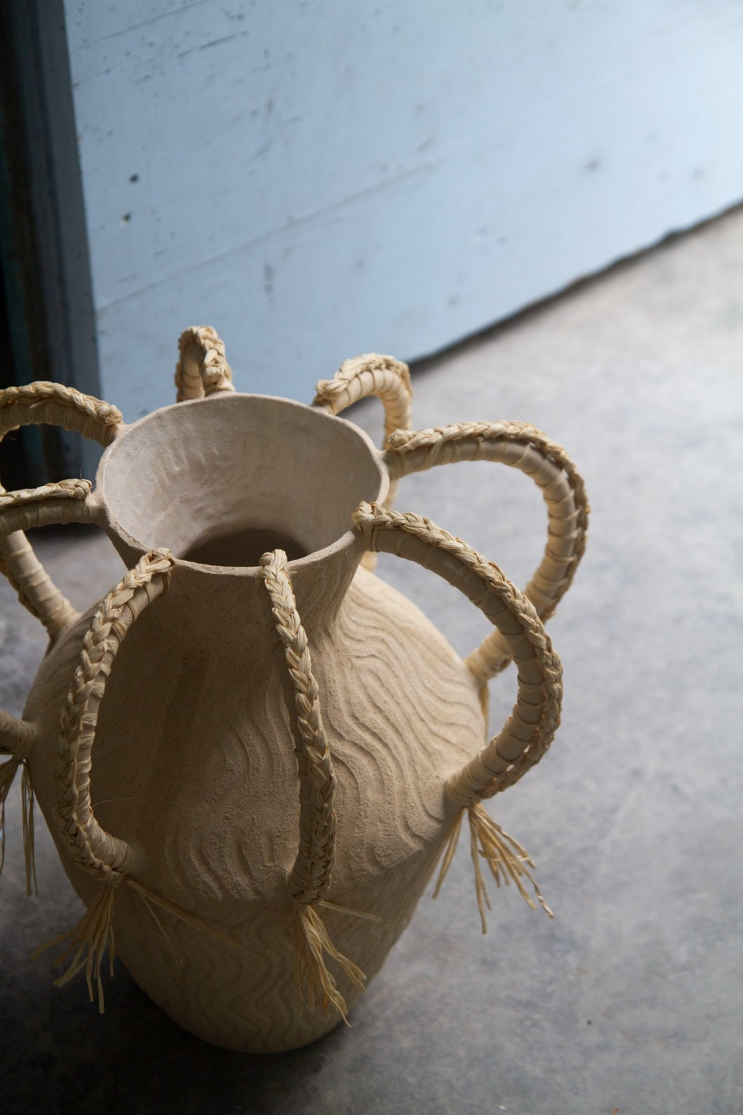 Amphora Ondas by Clandestine Céramique, handbuilt in sandy clay with engraved wave patterns and eight braided raphia handles, part of the House of Woven Stories selection.