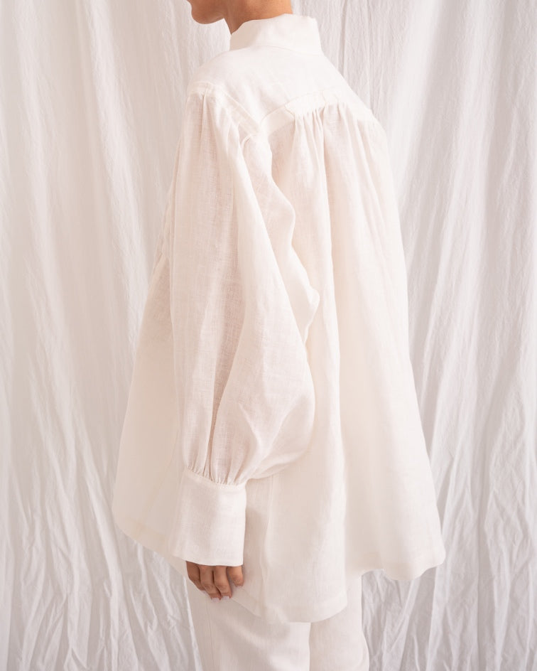 Model is wearing the Ancestral White Linen Shirt by Les Vacances d’Irina, a unisex handmade linen shirt with relaxed cut, open V-neckline, and natural shell buttons, crafted in Bucharest and available at House of Woven Stories.