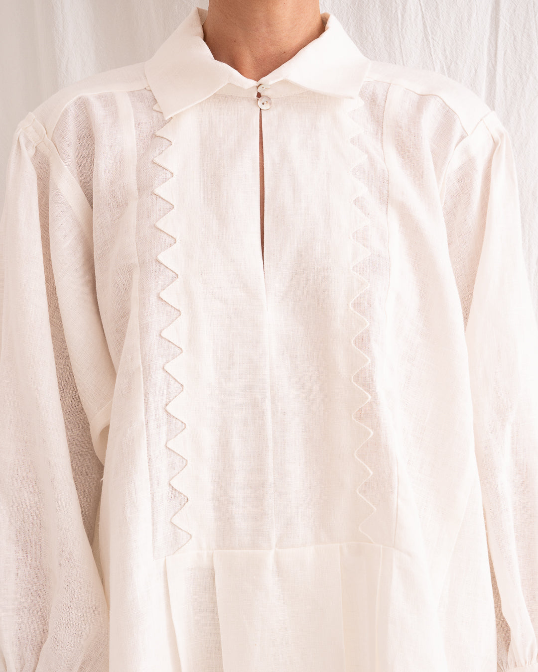 Model is wearing the Ancestral White Linen Shirt by Les Vacances d’Irina, a unisex handmade linen shirt with relaxed cut, open V-neckline, and natural shell buttons, crafted in Bucharest and available at House of Woven Stories.