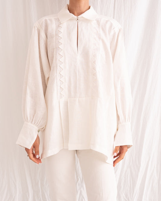 Model is wearing the Ancestral White Linen Shirt by Les Vacances d’Irina, a unisex handmade linen shirt with relaxed cut, open V-neckline, and natural shell buttons, crafted in Bucharest and available at House of Woven Stories.