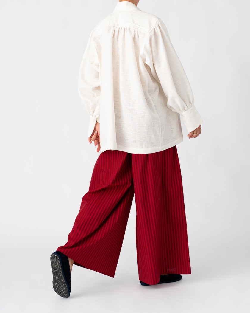 Model is wearing the Ancestral White Linen Shirt by Les Vacances d’Irina, a unisex handmade linen shirt with relaxed cut, open V-neckline, and natural shell buttons, crafted in Bucharest and available at House of Woven Stories.