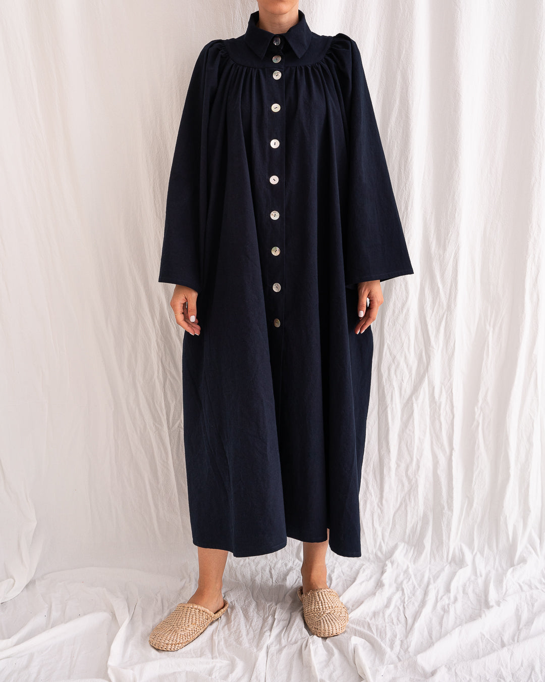 A Bigger Splash Cotton Dress by Les Vacances d’Irina, full-length long-sleeved maxi dress in ivory cotton with shell buttons, high collar, and hidden side pockets, handmade in Romania.