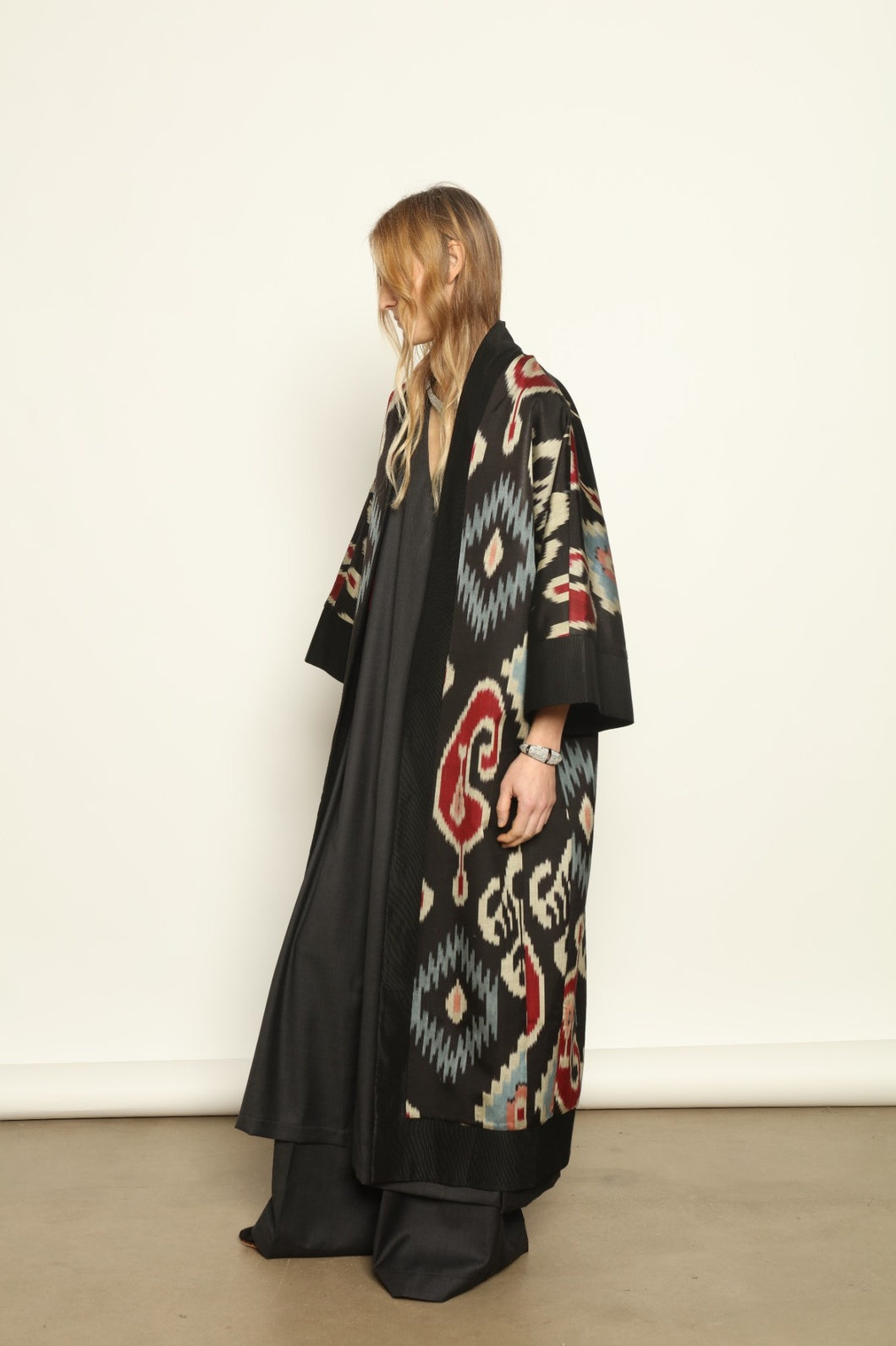 Model is wearing the Aura XL Ikat Silk Coat by Aleksandra Viktor, part of House of Woven Stories collection, handwoven Uzbek ikat silk coat with XL silhouette, expressive ikat motifs, and deep red lining