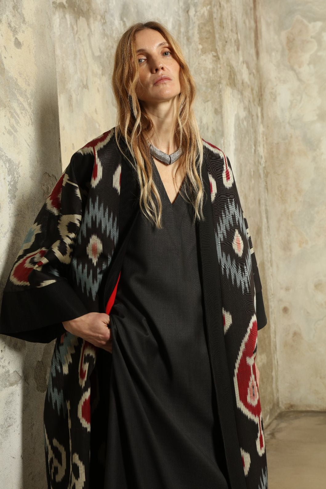 Model is wearing the Aura XL Ikat Silk Coat by Aleksandra Viktor, part of House of Woven Stories collection, handwoven Uzbek ikat silk coat with XL silhouette, expressive ikat motifs, and deep red lining