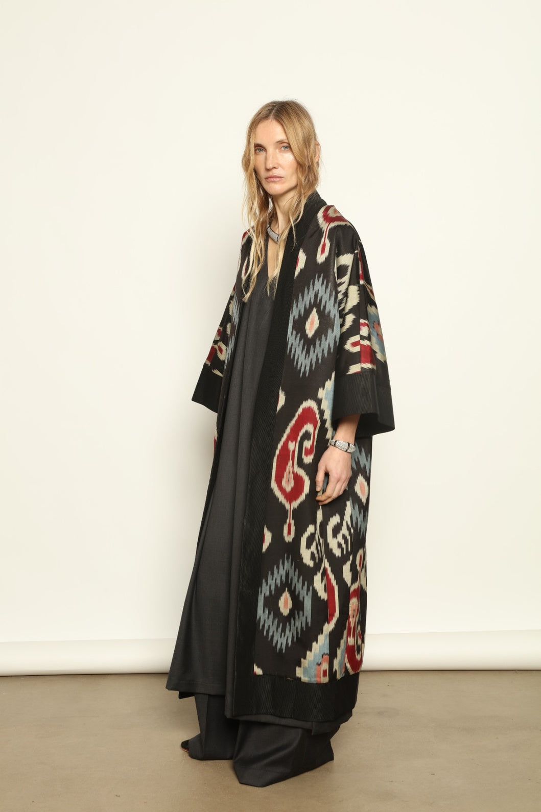 Model is wearing the Aura XL Ikat Silk Coat by Aleksandra Viktor, part of House of Woven Stories collection, handwoven Uzbek ikat silk coat with XL silhouette, expressive ikat motifs, and deep red lining