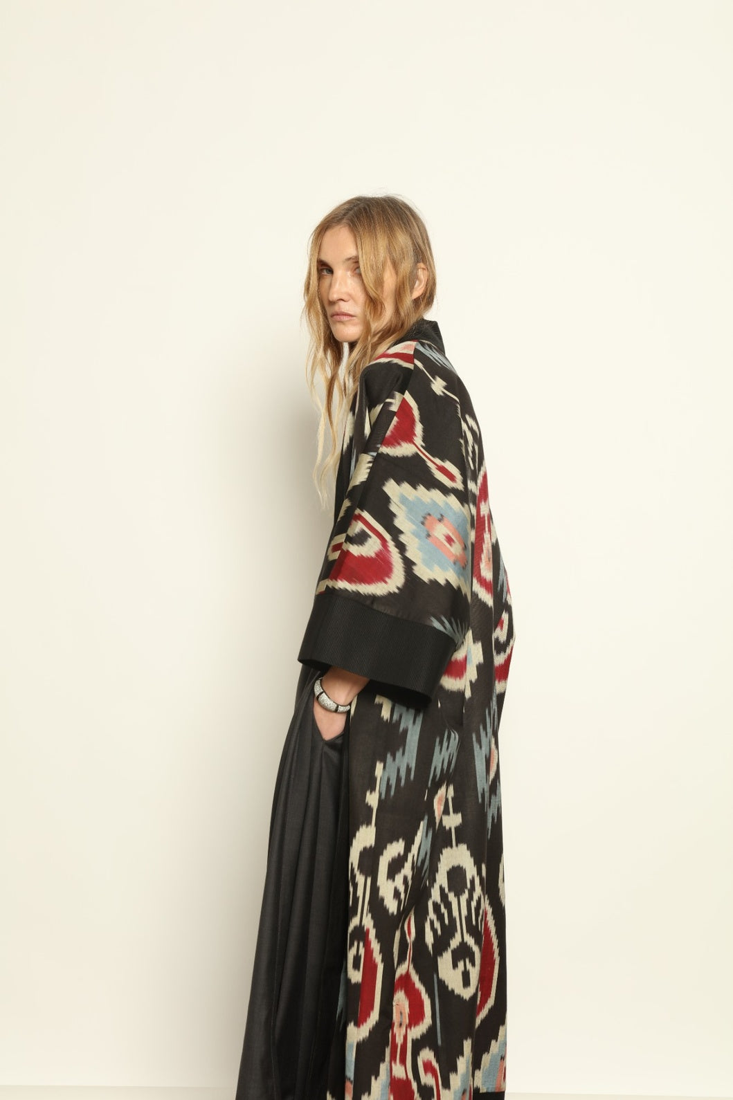 Model is wearing the Aura XL Ikat Silk Coat by Aleksandra Viktor, part of House of Woven Stories collection, handwoven Uzbek ikat silk coat with XL silhouette, expressive ikat motifs, and deep red lining