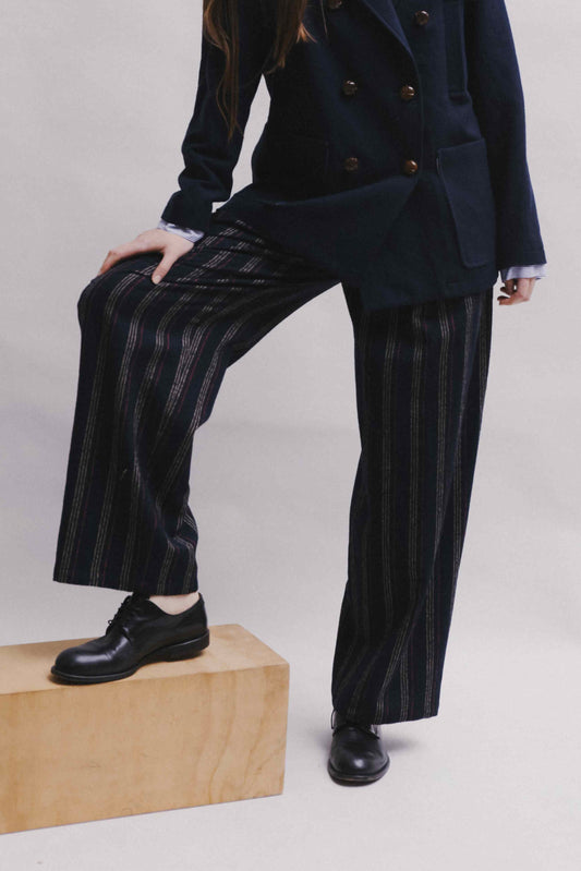 Model is wearing Balia 8.22 navy blue striped trousers made from virgin wool and cotton, tailored fit, Italian craftsmanship, part of House of Woven Stories selection.