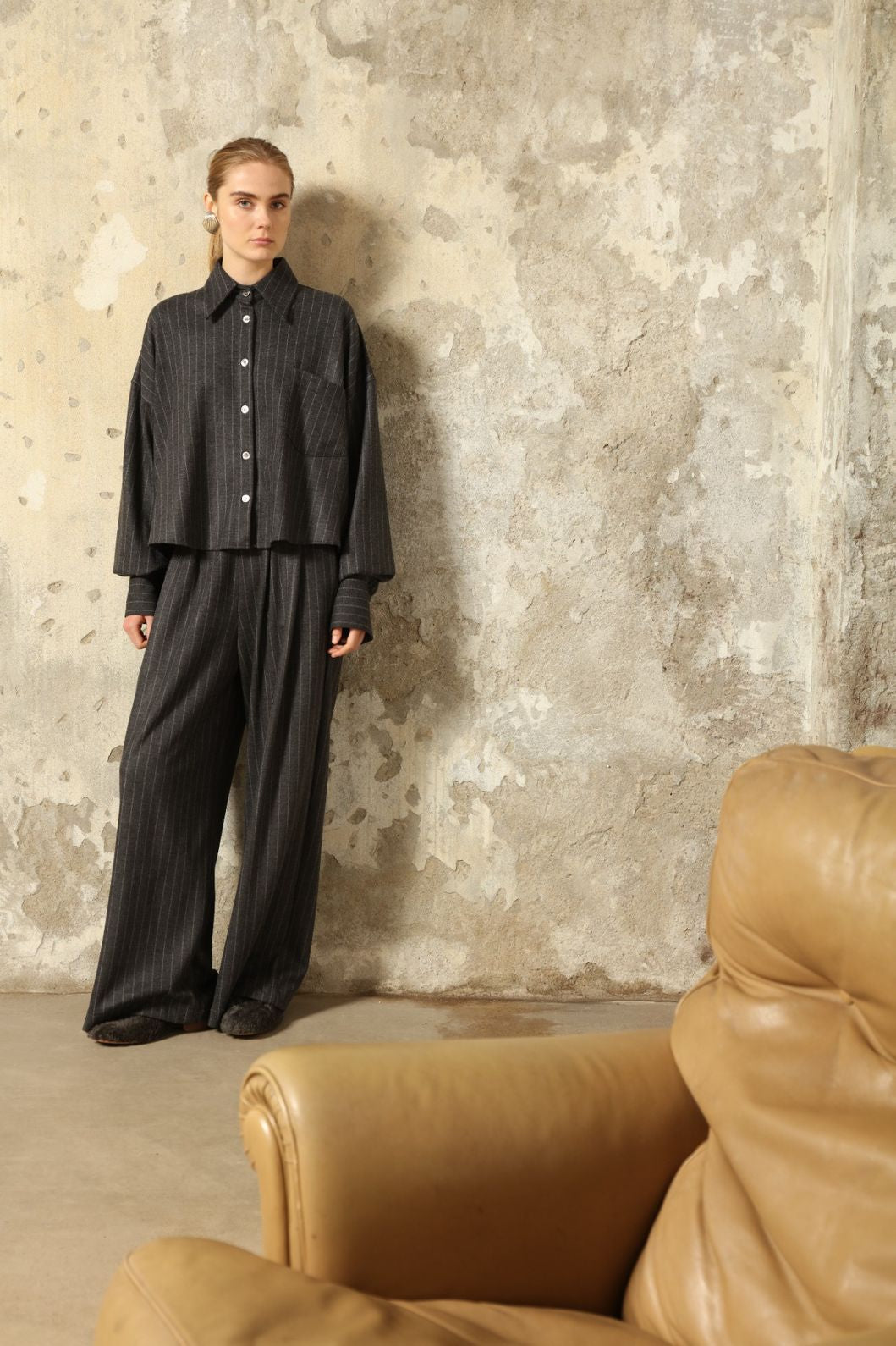 Model is wearing Bettina Striped Grey and White Double Jersey Shirt by House of Woven Stories, part of the curated selection, handcrafted in Italy from linen, wool, and silk blend with vertical stripes, relaxed tailoring, and fluid drape for timeless elegance.