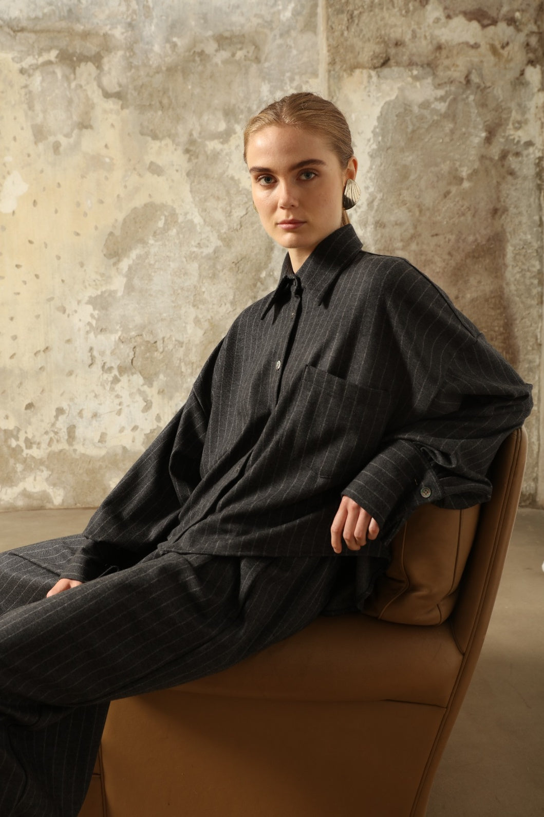Model is wearing Bettina Striped Grey and White Double Jersey Shirt by House of Woven Stories, part of the curated selection, handcrafted in Italy from linen, wool, and silk blend with vertical stripes, relaxed tailoring, and fluid drape for timeless elegance.