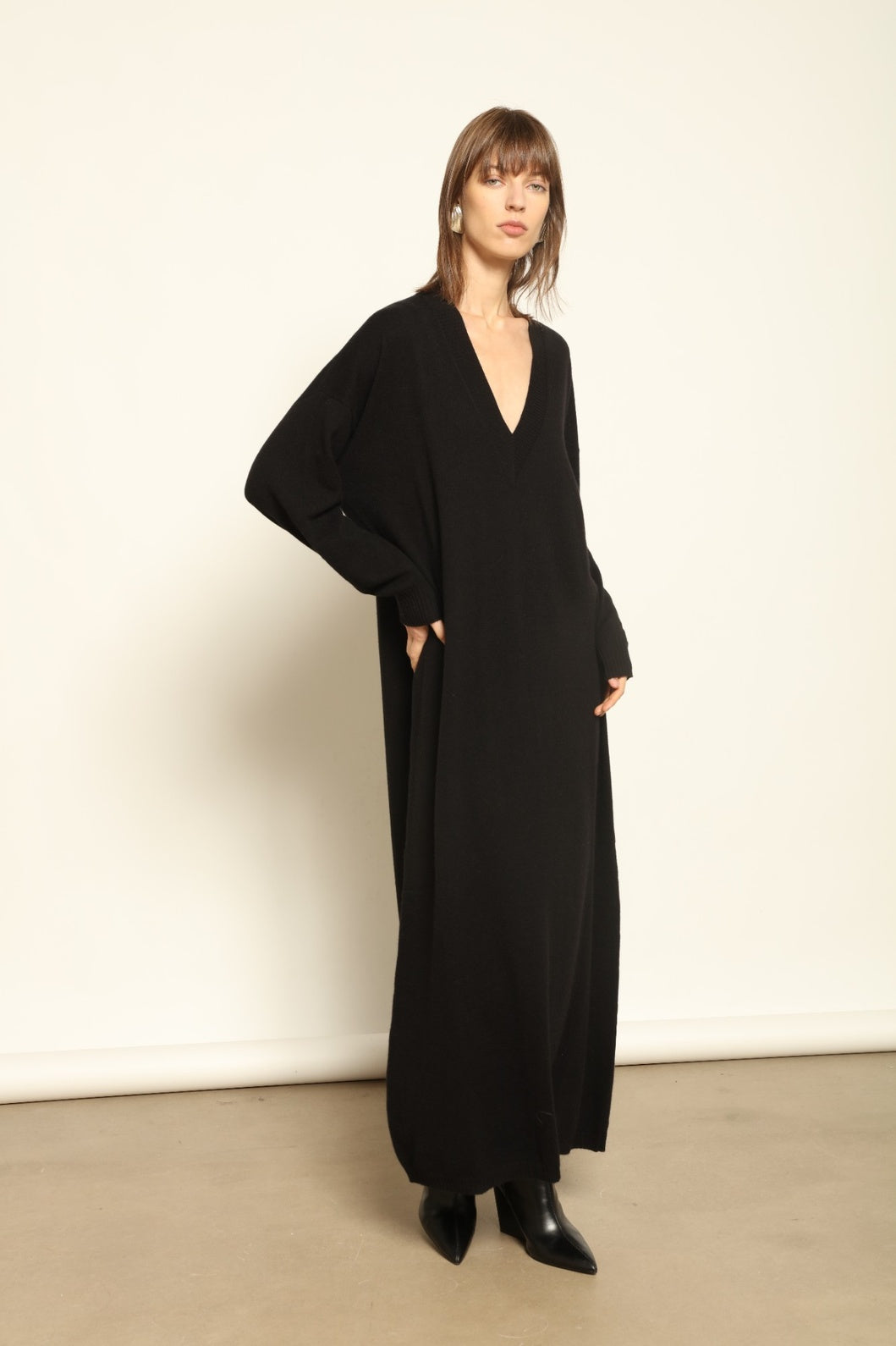 Model wearing the Black Katharina V-Neck Cashmere Maxi Dress by House of Woven Stories, crafted in Italy from 100% pure Inner Mongolia cashmere, featuring a flowing silhouette, soft drape, and timeless sustainable black knitwear design