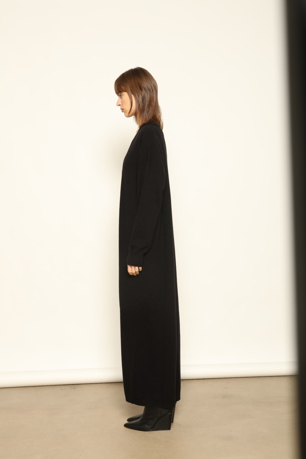 Model wearing the Black Katharina V-Neck Cashmere Maxi Dress by House of Woven Stories, crafted in Italy from 100% pure Inner Mongolia cashmere, featuring a flowing silhouette, soft drape, and timeless sustainable black knitwear design