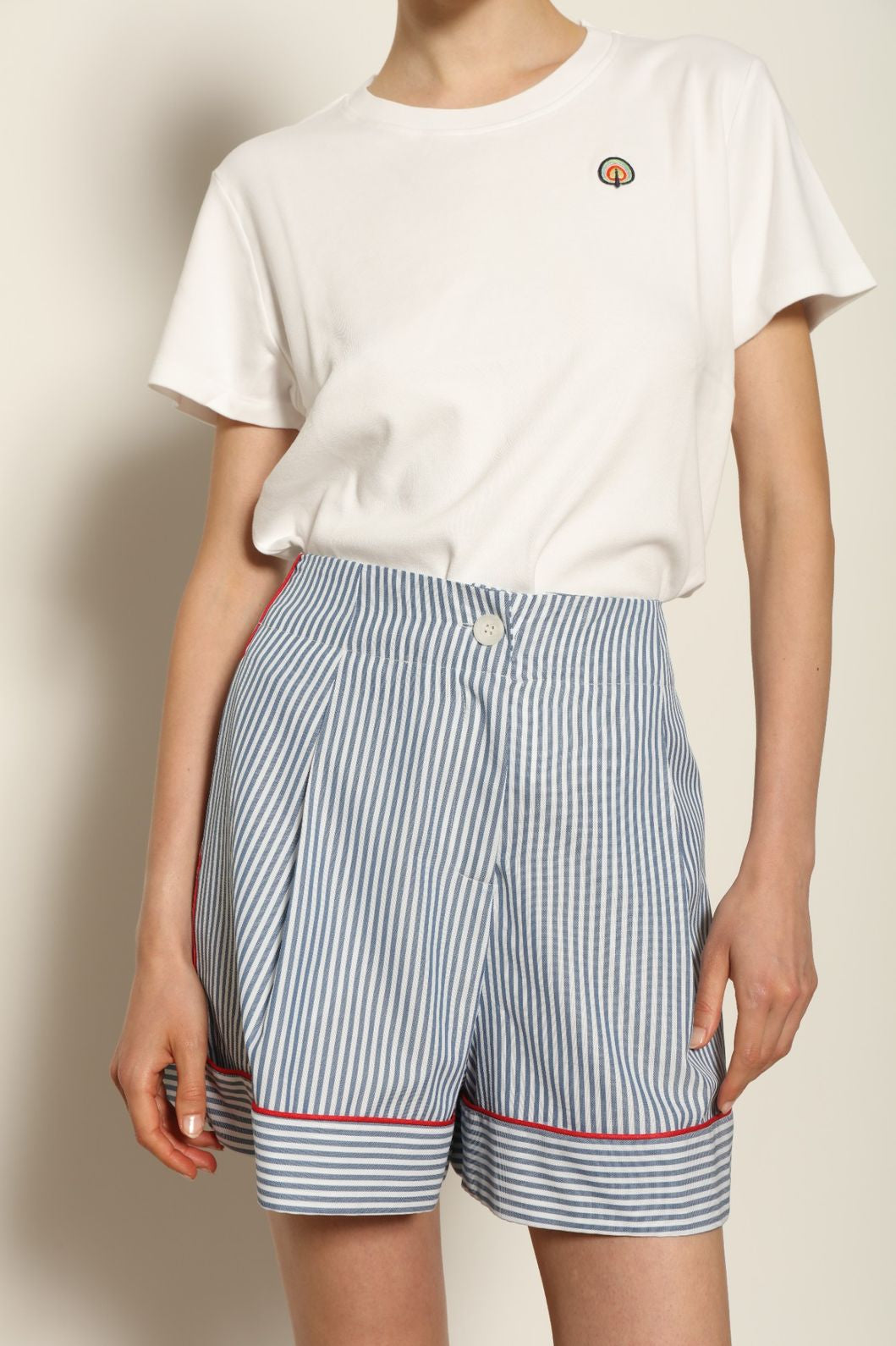 Model is wearing blue and white striped 100% cotton shorts with contrasting red piping by House of Woven Stories. The shorts feature a relaxed, tailored silhouette designed for comfort and ease of movement. Made in Italy from premium natural cotton, they reflect artisan craftsmanship and timeless warm-weather style, styled as part of a contemporary resort wear look.