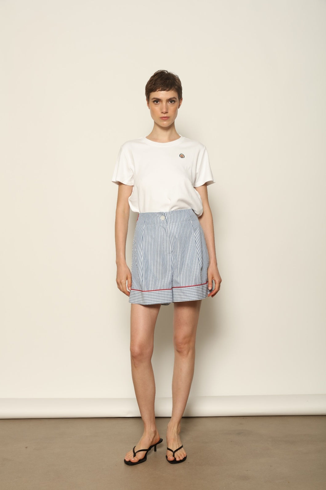 Model is wearing blue and white striped 100% cotton shorts with contrasting red piping by House of Woven Stories. The shorts feature a relaxed, tailored silhouette designed for comfort and ease of movement. Made in Italy from premium natural cotton, they reflect artisan craftsmanship and timeless warm-weather style, styled as part of a contemporary resort wear look.