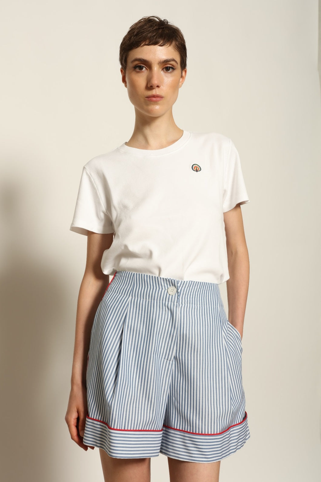 Model is wearing blue and white striped 100% cotton shorts with contrasting red piping by House of Woven Stories. The shorts feature a relaxed, tailored silhouette designed for comfort and ease of movement. Made in Italy from premium natural cotton, they reflect artisan craftsmanship and timeless warm-weather style, styled as part of a contemporary resort wear look.