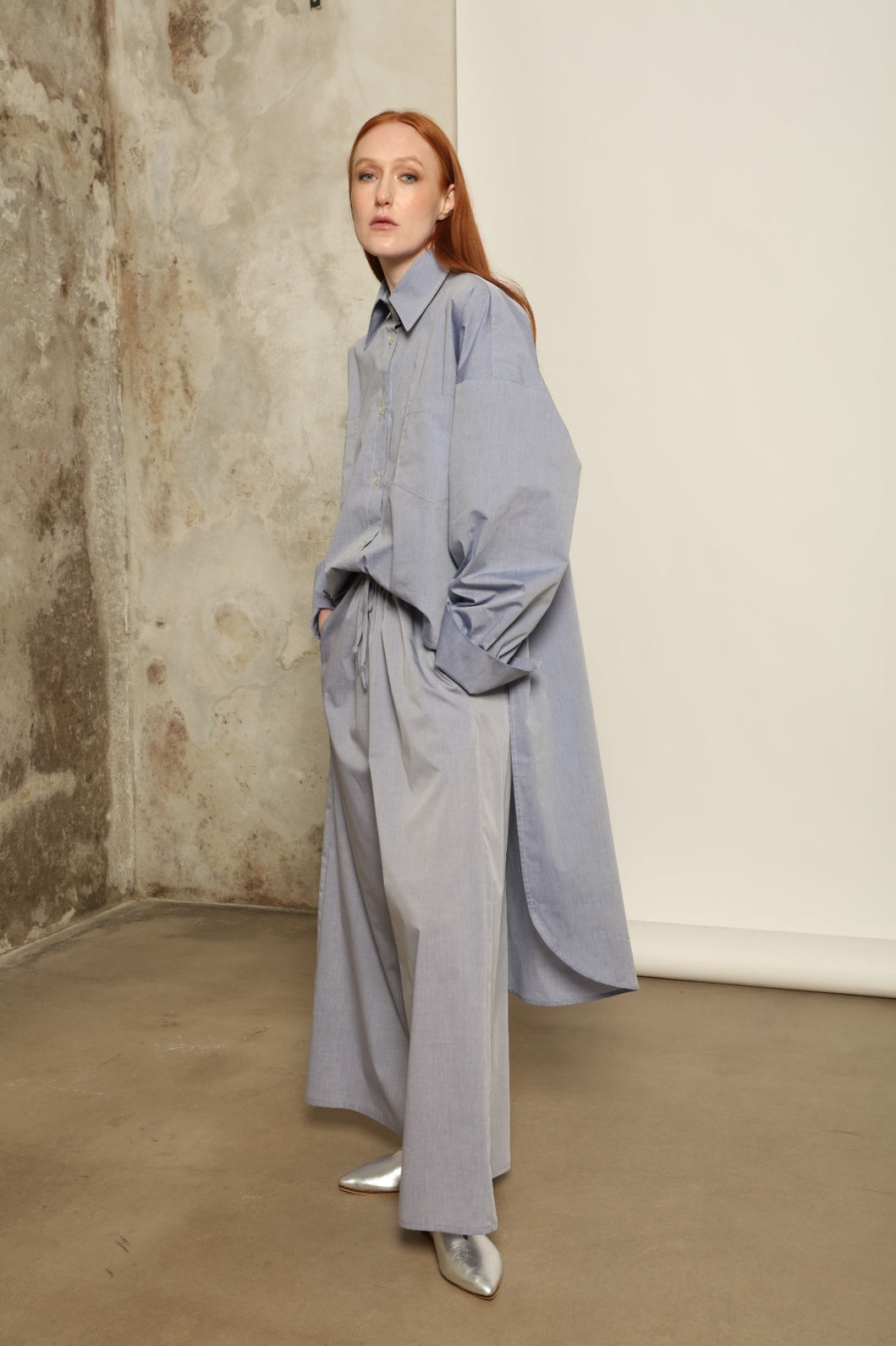 Model is wearing the Brigitta dusty blue cotton mousseline trousers from the House of Woven Stories selection, lightweight and breathable women’s summer pants made in Italy in Piedmont, crafted from 100% natural cotton with a relaxed tailored silhouette designed for effortless movement.