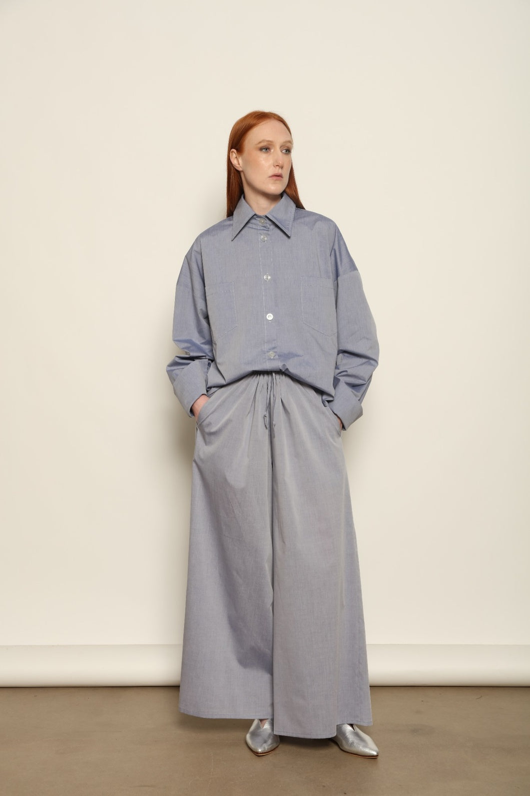 Model is wearing the Brigitta dusty blue cotton mousseline trousers from the House of Woven Stories selection, lightweight and breathable women’s summer pants made in Italy in Piedmont, crafted from 100% natural cotton with a relaxed tailored silhouette designed for effortless movement.