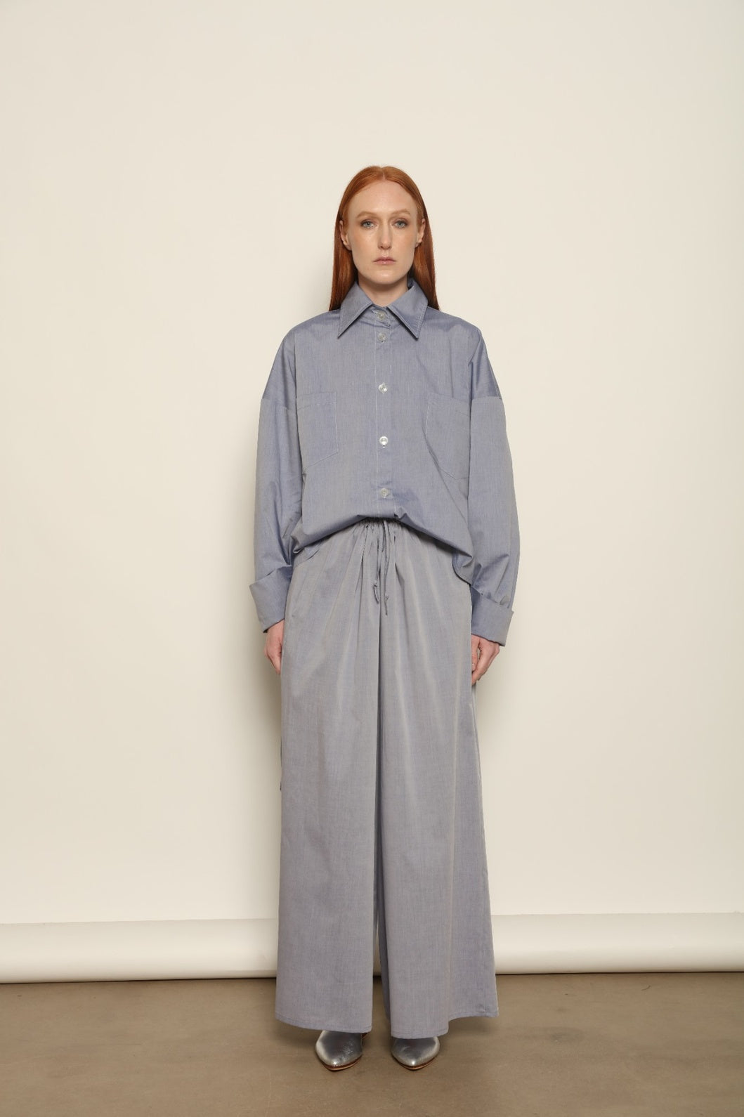 Model is wearing the Brigitta dusty blue cotton mousseline trousers from the House of Woven Stories selection, lightweight and breathable women’s summer pants made in Italy in Piedmont, crafted from 100% natural cotton with a relaxed tailored silhouette designed for effortless movement.