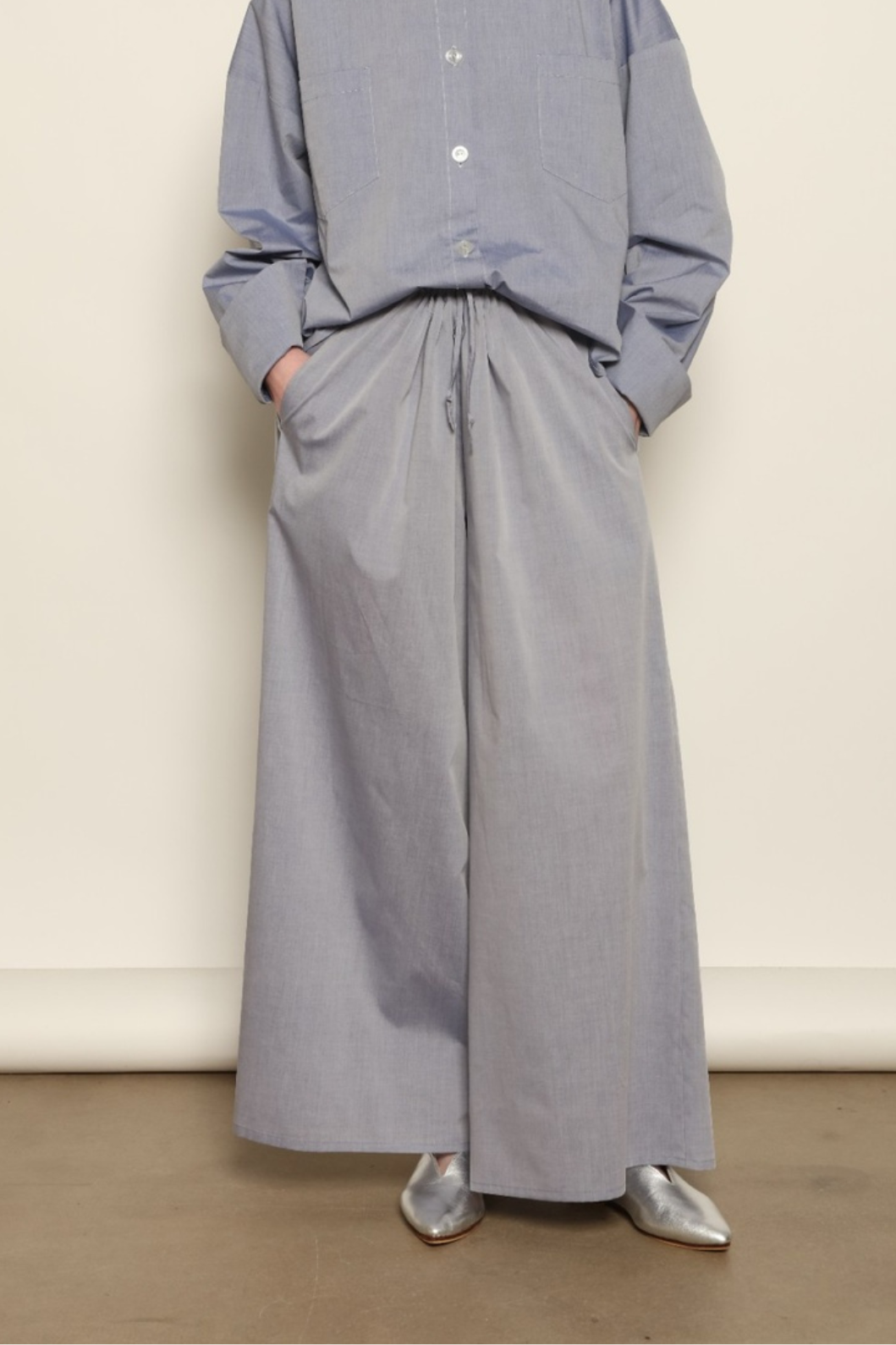 Model is wearing the Brigitta dusty blue cotton mousseline trousers from the House of Woven Stories selection, lightweight and breathable women’s summer pants made in Italy in Piedmont, crafted from 100% natural cotton with a relaxed tailored silhouette designed for effortless movement.
