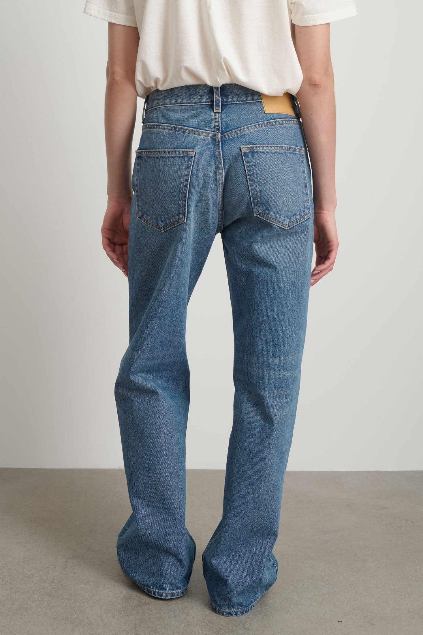 Model is wearing Bec Cotton Jean Halle Wash by B Sides in pale blue stone washed cotton denim with mid-rise straight leg fit, zip fly and brass button closure, available at House of Nomad Stories