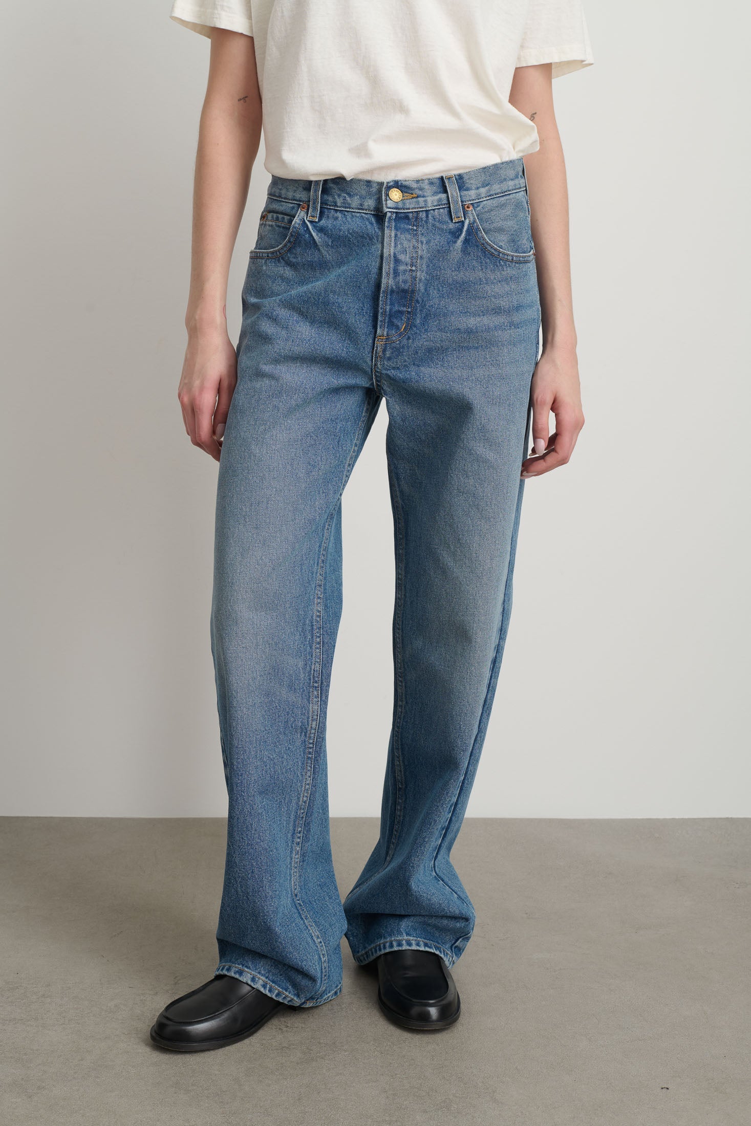 Model is wearing Bec Cotton Jean Halle Wash by B Sides in pale blue stone washed cotton denim with mid-rise straight leg fit, zip fly and brass button closure, available at House of Nomad Stories