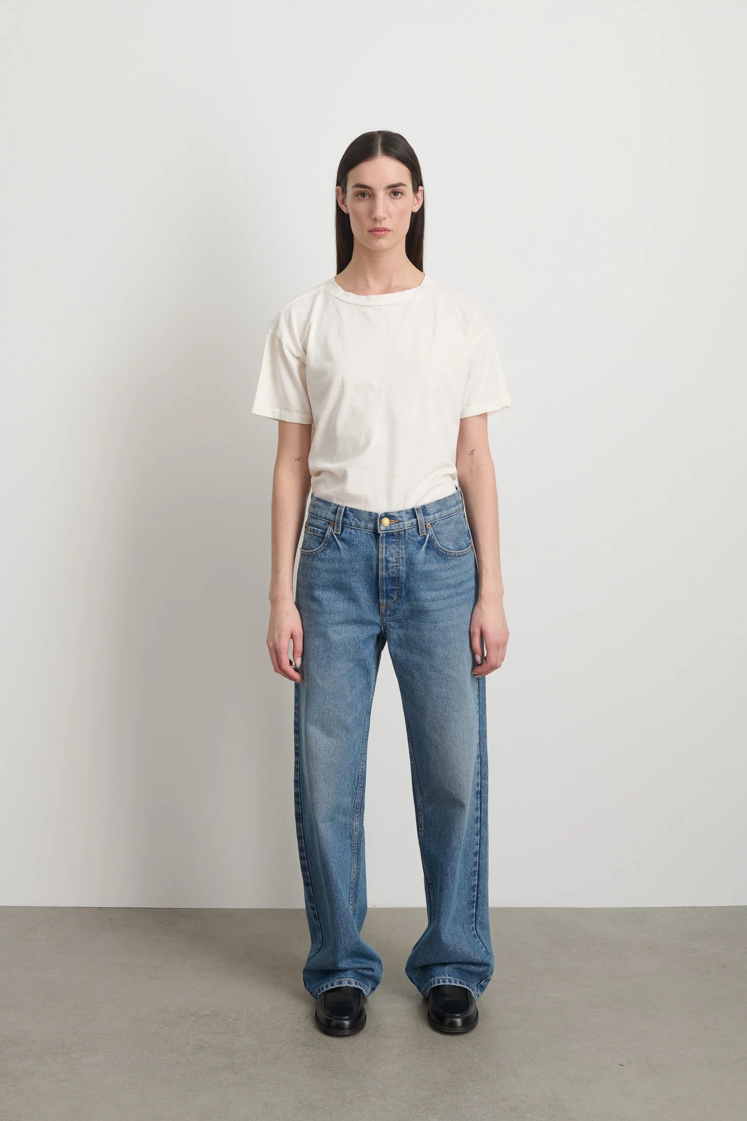 Model is wearing Bec Cotton Jean Halle Wash by B Sides in pale blue stone washed cotton denim with mid-rise straight leg fit, zip fly and brass button closure, available at House of Nomad Stories