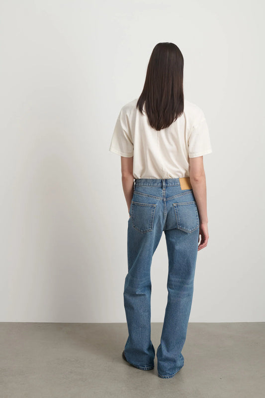 Model is wearing Bec Cotton Jean Halle Wash by B Sides in pale blue stone washed cotton denim with mid-rise straight leg fit, zip fly and brass button closure, available at House of Nomad Stories