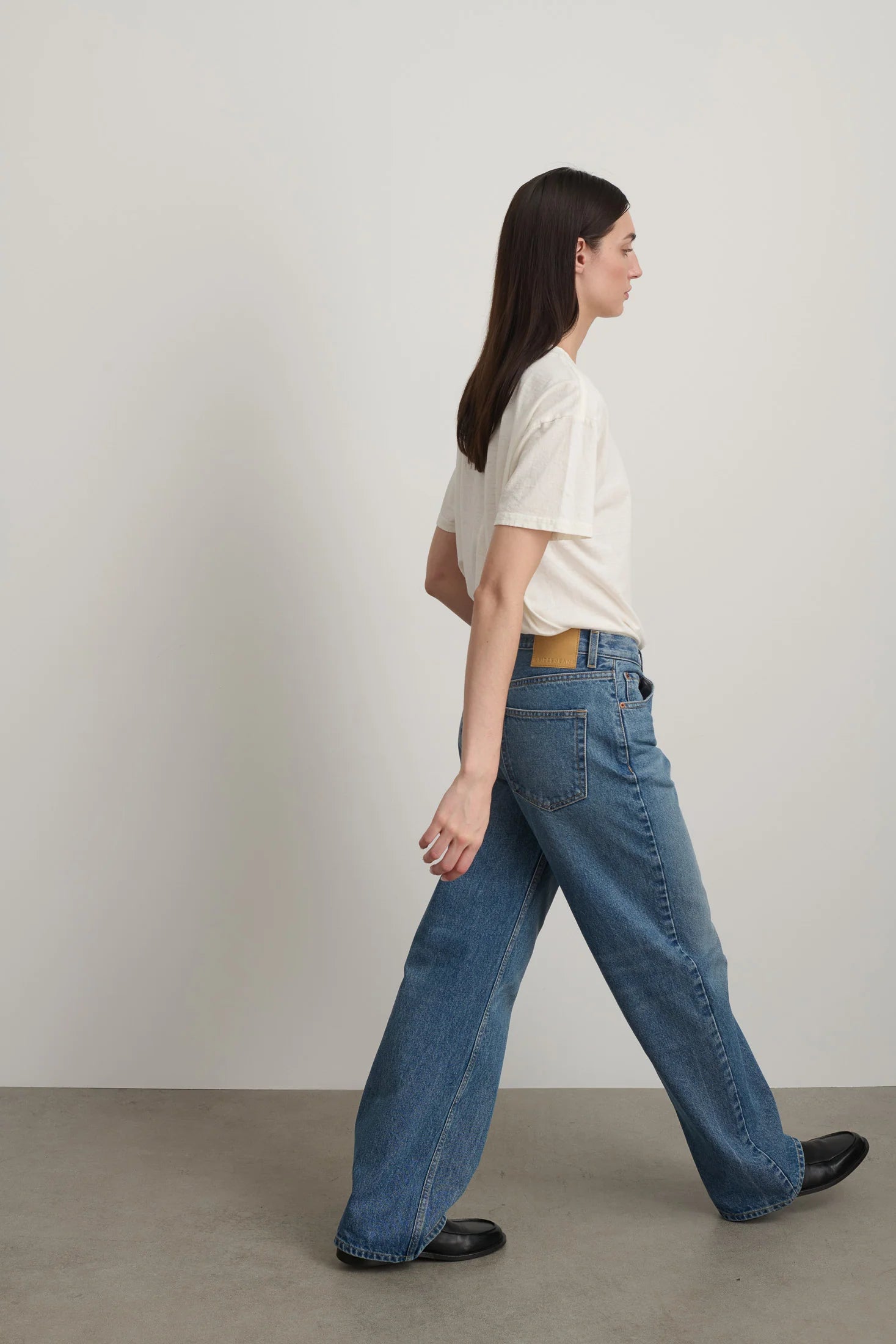 Model is wearing Bec Cotton Jean Halle Wash by B Sides in pale blue stone washed cotton denim with mid-rise straight leg fit, zip fly and brass button closure, available at House of Nomad Stories