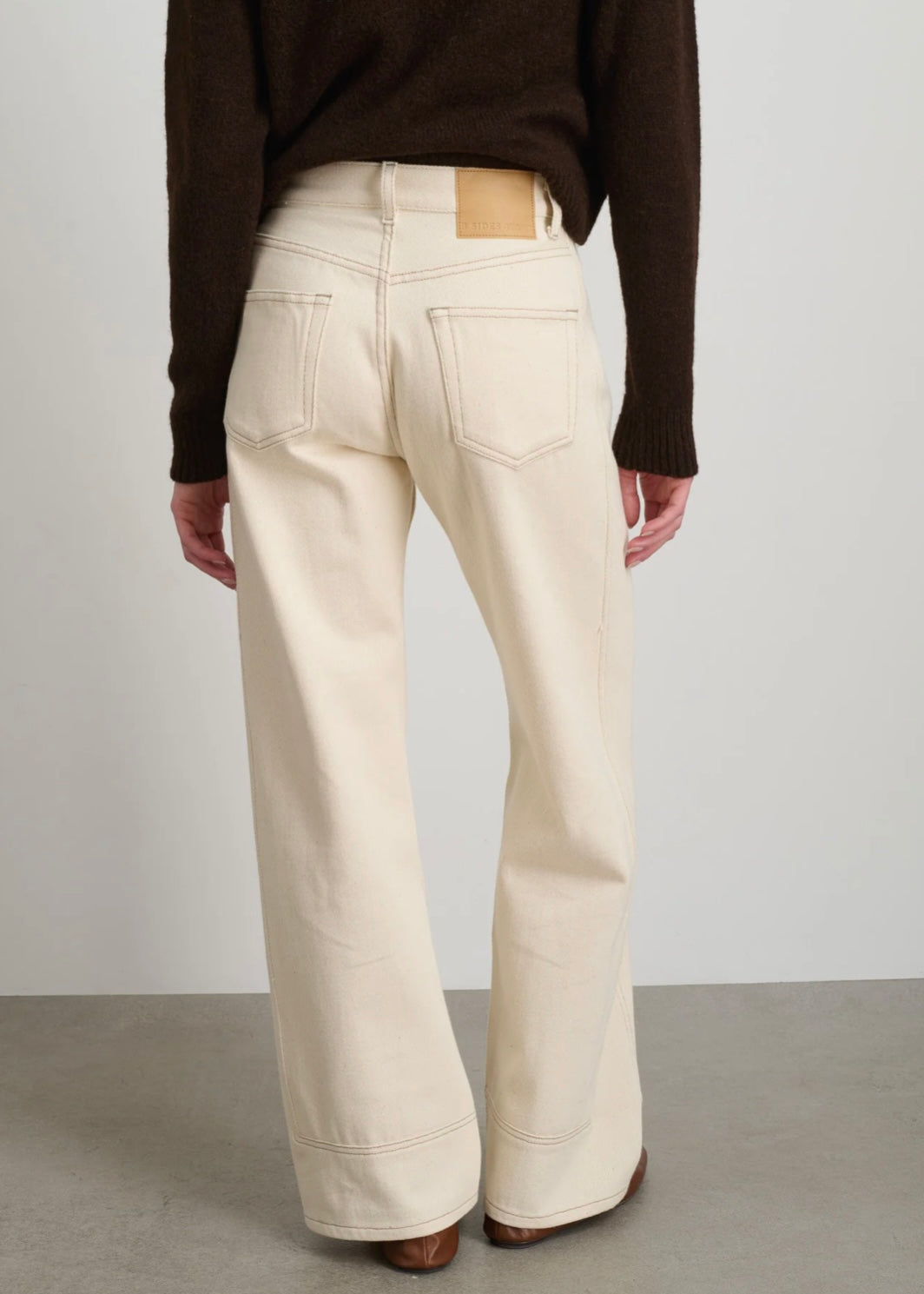Model is wearing B Sides Charlot jeans, mid-rise relaxed straight denim in undyed cotton, with 5-pocket design, copper rivets, and brass logo button, part of the House of Woven Stories curated collection.