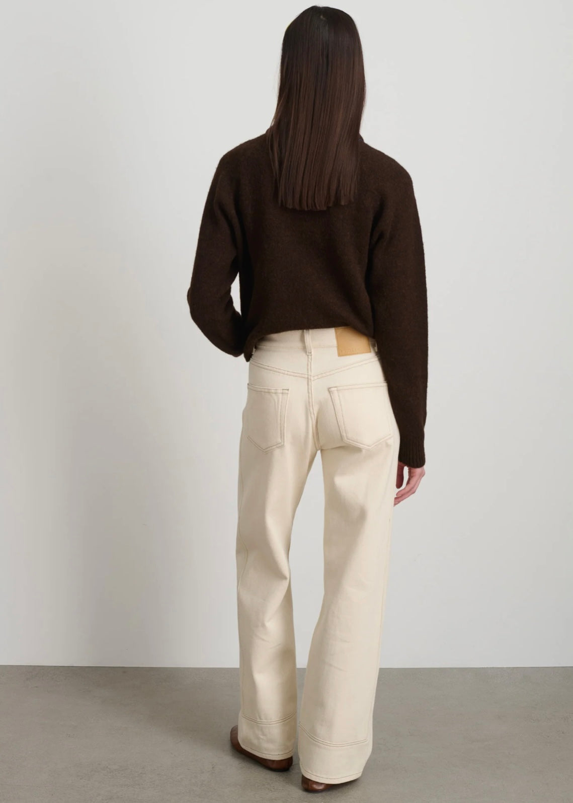 Model is wearing B Sides Charlot jeans, mid-rise relaxed straight denim in undyed cotton, with 5-pocket design, copper rivets, and brass logo button, part of the House of Woven Stories curated collection.