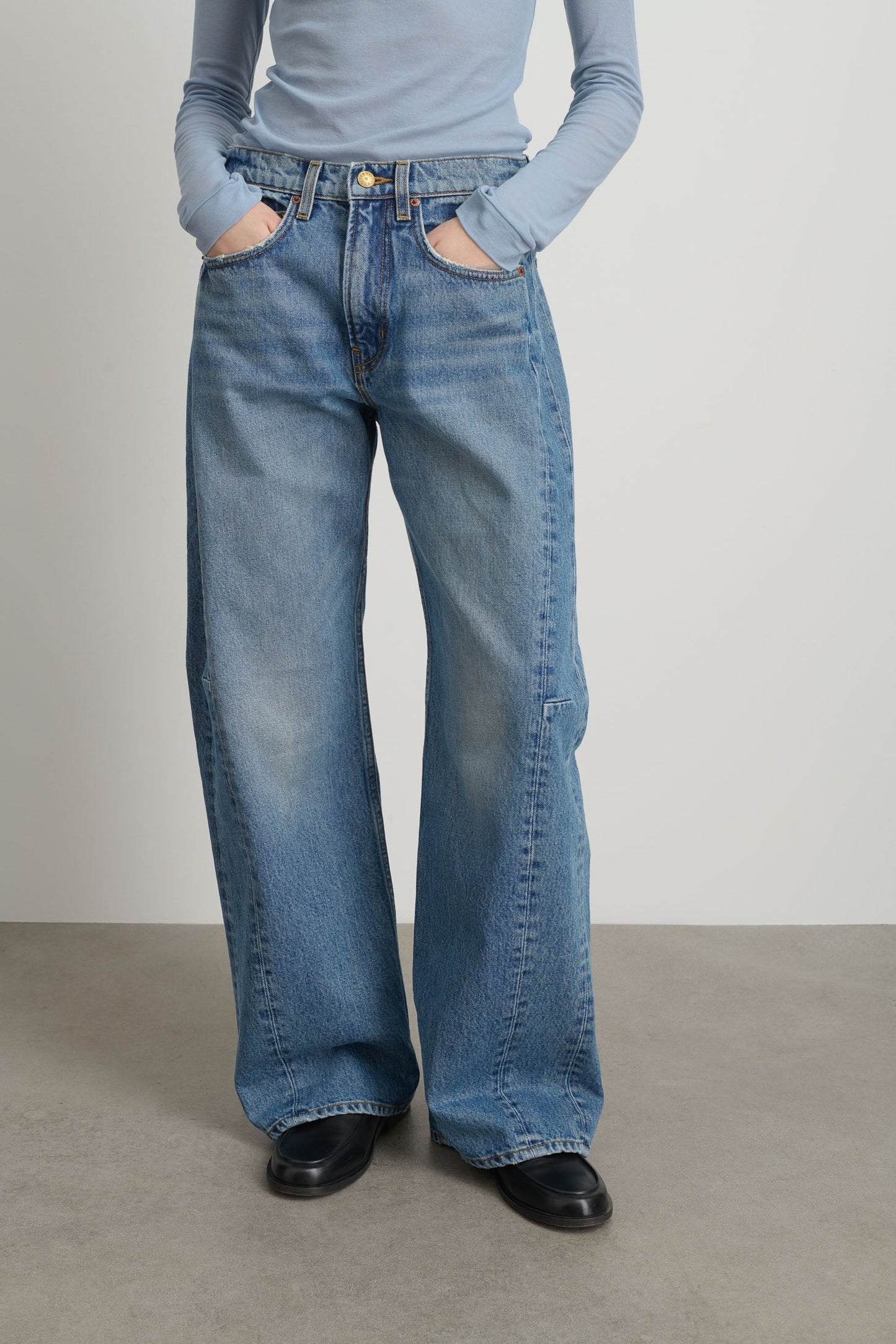 Model is wearing Relaxed Cuffed Lasso Jean Jane Wash by B Sides in pale blue stone washed cotton-rich denim with high waist, pieced outseam, kinked leg and raw hem, available at House of Nomad Stories