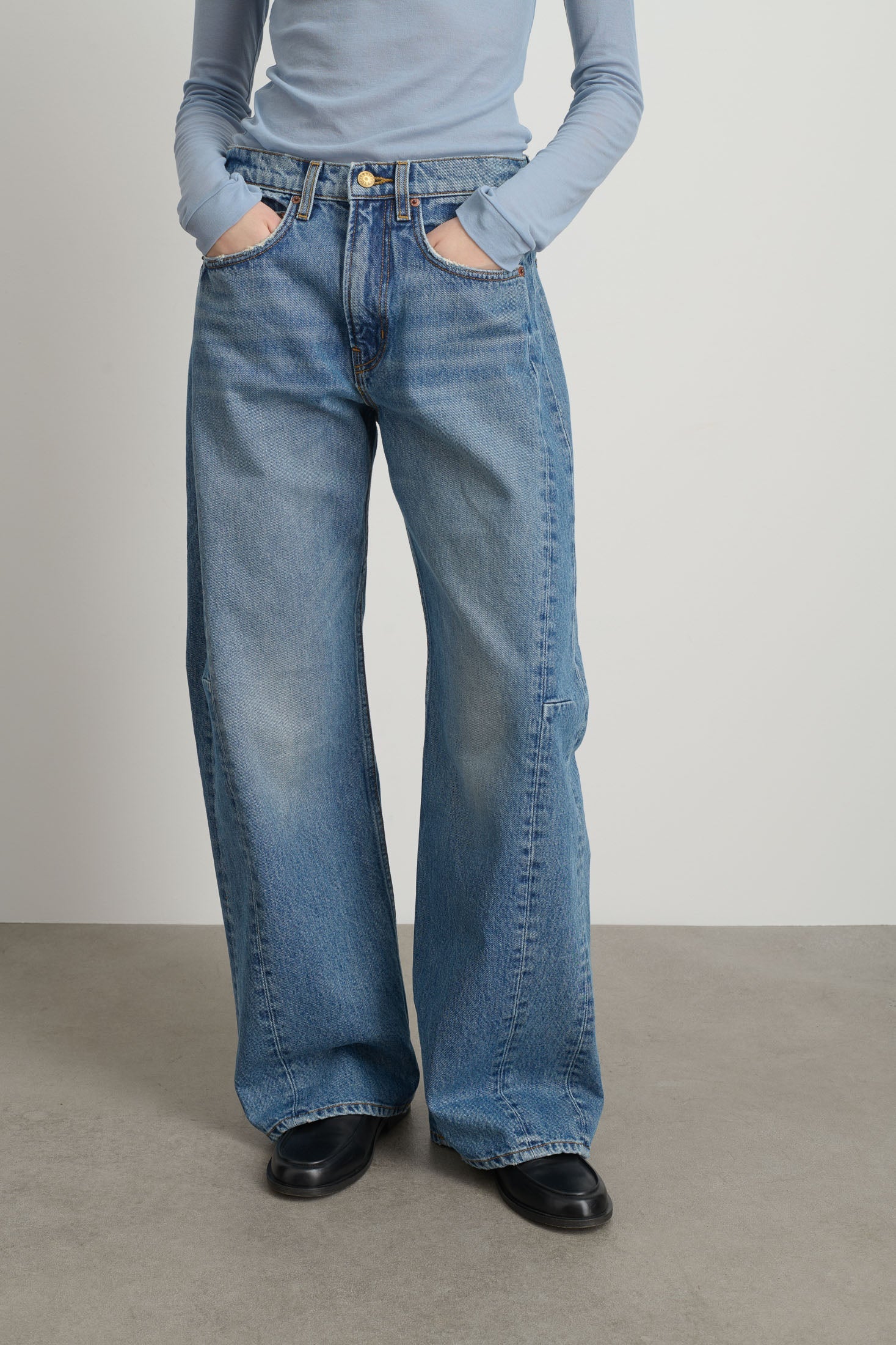 Model is wearing Relaxed Cuffed Lasso Jean Jane Wash by B Sides in pale blue stone washed cotton-rich denim with high waist, pieced outseam, kinked leg and raw hem, available at House of Nomad Stories