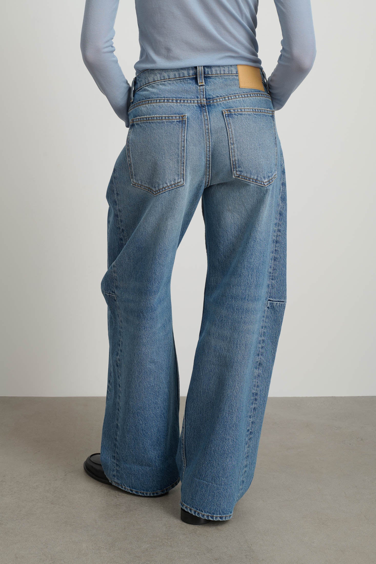 Model is wearing Relaxed Cuffed Lasso Jean Jane Wash by B Sides in pale blue stone washed cotton-rich denim with high waist, pieced outseam, kinked leg and raw hem, available at House of Nomad Stories