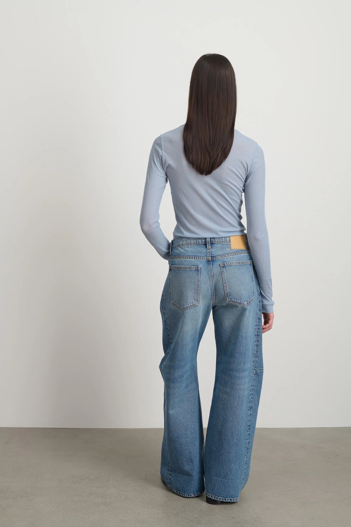 Model is wearing Relaxed Cuffed Lasso Jean Jane Wash by B Sides in pale blue stone washed cotton-rich denim with high waist, pieced outseam, kinked leg and raw hem, available at House of Nomad Stories