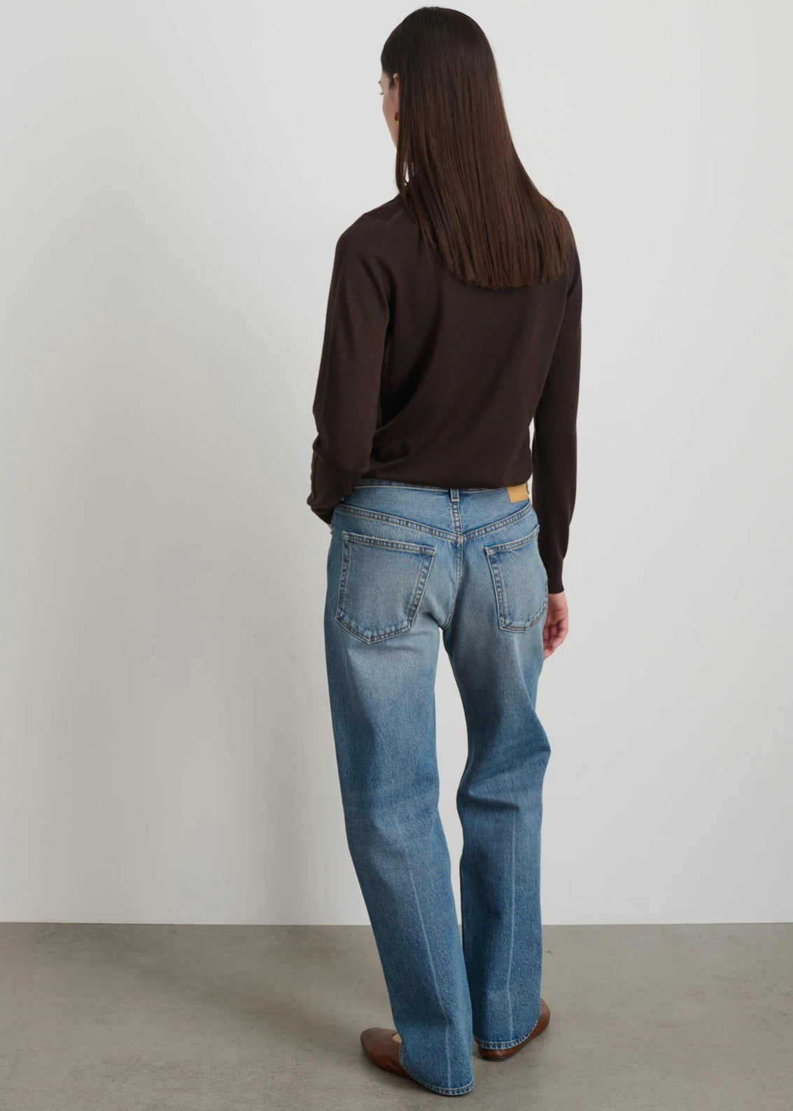 Model is wearing B Sides Tilda Jeans, mid-rise draped straight indigo denim with curved inseam, tapered leg, zip fly, and brass button, part of House of Woven Stories curated collection.