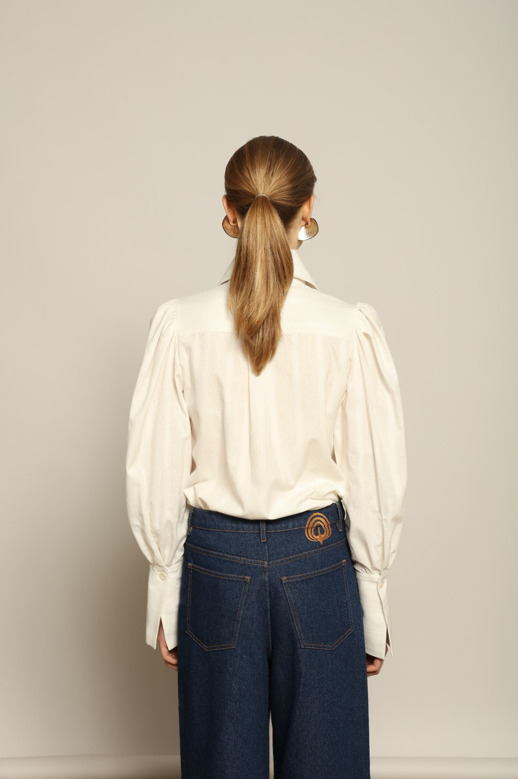 Model is wearing the Chantilly Karin Pure Cotton Blouse by House of Woven Stories, crafted from 100% cotton with a statement collar, delicate pleating at the shoulders, and extended cuffs, combining timeless elegance with modern tailoring.