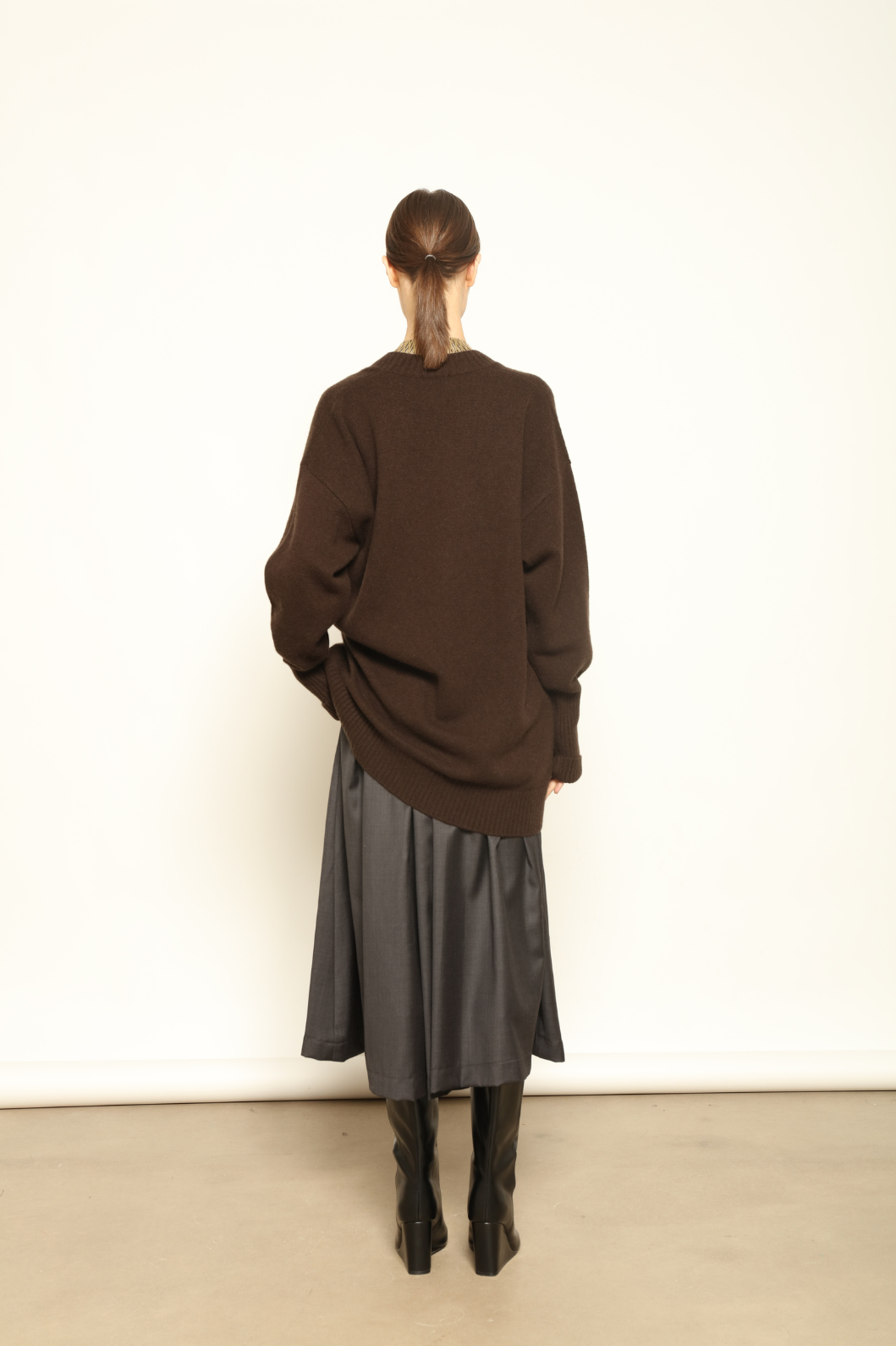 Model is wearing the Chocolate Nina V-Neck Long Sweater by House of Woven Stories, crafted from 100% pure Inner Mongolia cashmere in a deep chocolate shade, featuring an elongated silhouette, deep V-neckline, soft breathable knit, and timeless sustainable Italian luxury design