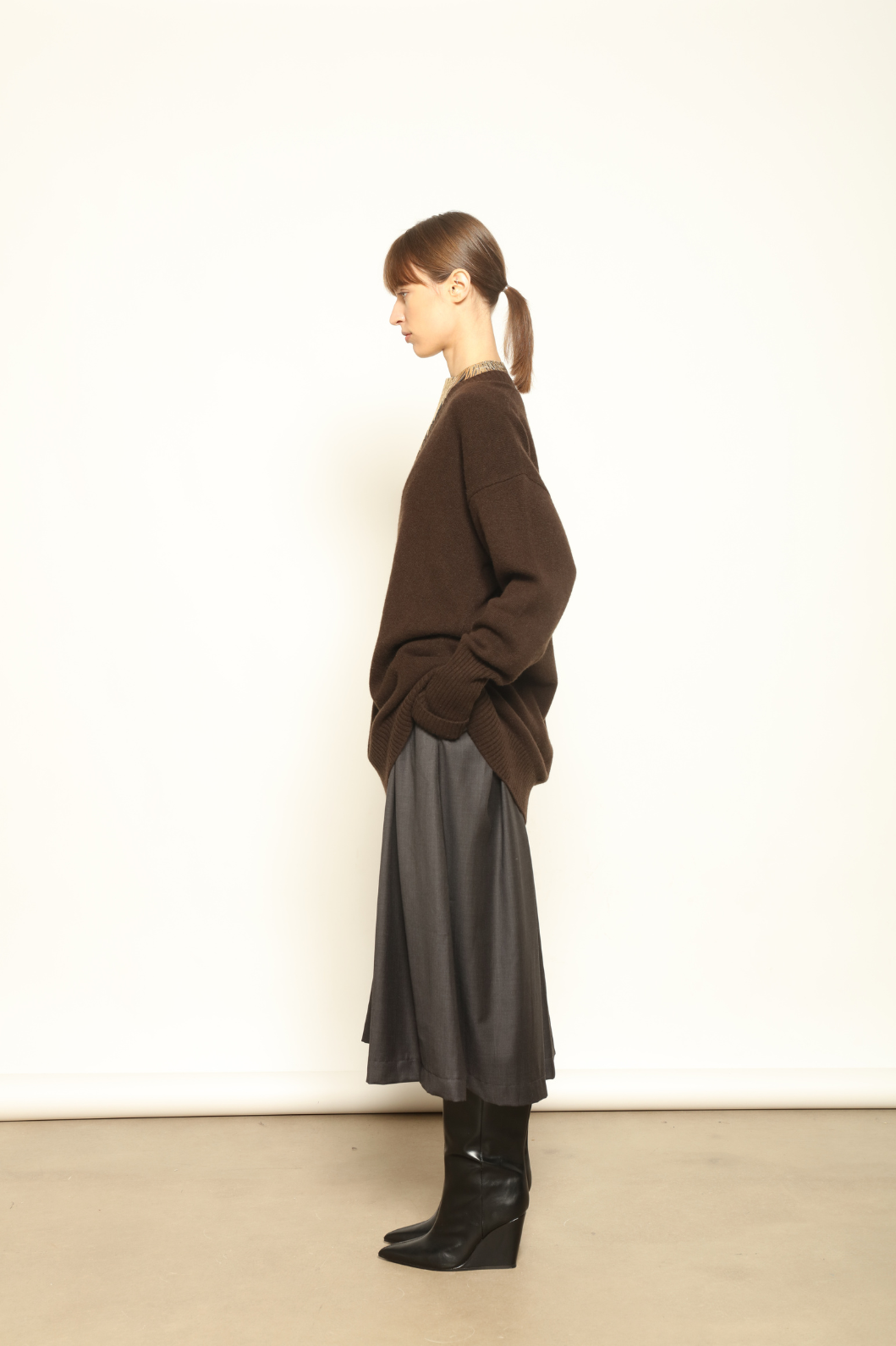 Model is wearing the Chocolate Nina V-Neck Long Sweater by House of Woven Stories, crafted from 100% pure Inner Mongolia cashmere in a deep chocolate shade, featuring an elongated silhouette, deep V-neckline, soft breathable knit, and timeless sustainable Italian luxury design